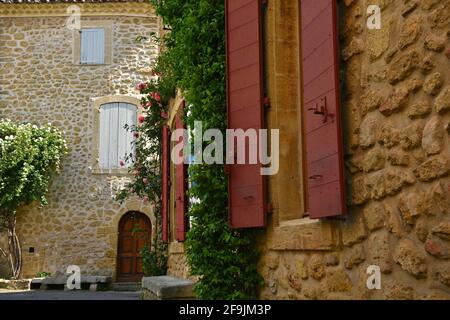 Typische Provençal-Stil Landhaussteinfassade mit roten hölzernen Fensterläden im malerischen Dorf Lourmarin in Vaucluse, Provence Frankreich. Stockfoto