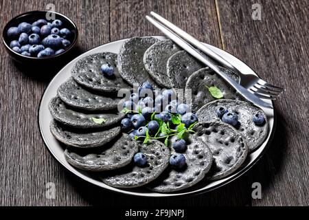 Süße Pfannkuchen mit Aktivkohle, serviert mit Heidelbeeren und Minze auf einem Teller auf einem Holztisch, Blick von oben Stockfoto