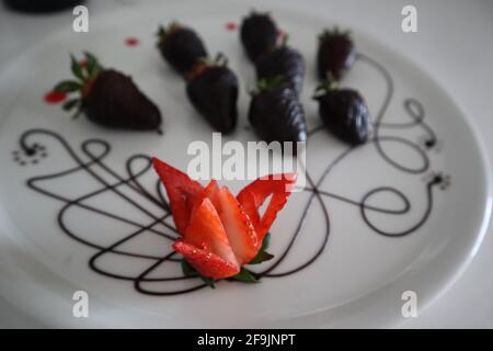 Nahaufnahme eines mit Schokolade überzogenen Erdbeeren-Dessert, rohe Erdbeere, die in eine Blume geschnitzt wurde Stockfoto