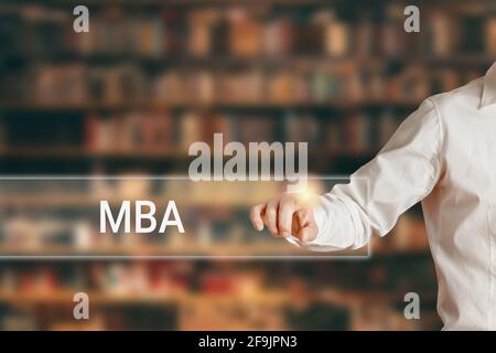 Männliche Hand drückt das Wort MBA auf einer virtuellen Suchanzeigeleiste vor Bibliothekshintergrund. Master of Business Administration Ausbildung. Stockfoto