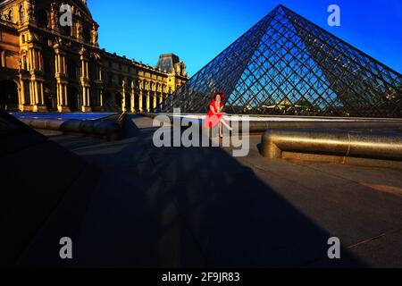 Paris, Frankreich, Louvre, sonniger Innenhof und Glaspalamide des Louvre in Paris in Frankreich mit sitzender Frau mit rotem Kleid und rotem Hut Stockfoto