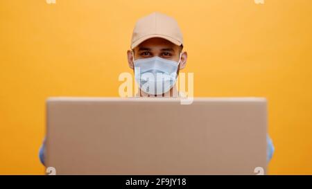 Erwachsene Mann mit Kappe, der eine chirurgische Gesichtsmaske trägt und Schutzhandschuhe trägt, die den Karton vor sich halten. Ort für Ihren Text. Die weltweite COVID-19-Pandemie. Stockfoto
