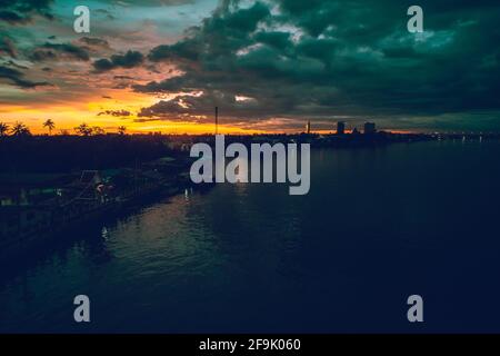 Panorama-Stadtbild bei Sonnenuntergang mit großem Fluss im Vordergrund und strommwolken im Hintergrund in Thailand. Stockfoto