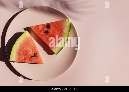 Frische rote Wassermelonenscheiben auf rosafarbenem Teller und tropischer Blattschatten. Stockfoto