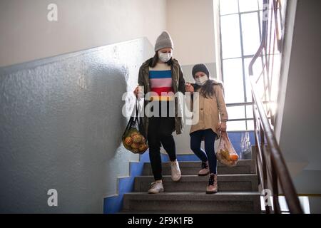 Mutter mit kleiner Tochter mit Einkaufstaschen auf der Treppe im Wohnblock, Coronavirus-Konzept. Stockfoto