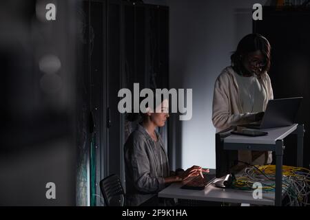 Porträt zweier weiblicher IT-Ingenieure, die im dunklen Serverraum mit Computer arbeiten, Kopierraum Stockfoto