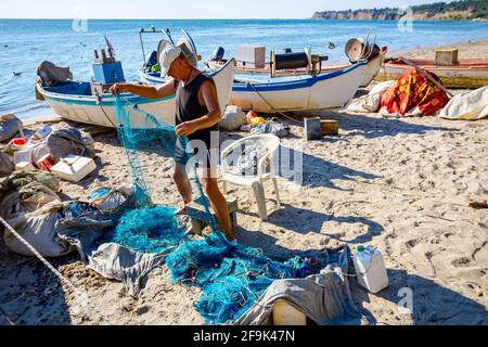 Fischer häufen Fischnetz und bereiten sich auf sein nächstes Angeln. Die Boote sind trocken am Sandstrand angedockt. Stockfoto