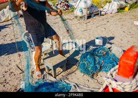 Fischer häufen Fischnetz auf dem Sandstrand und bereiten sich auf sein nächstes Angeln. Stockfoto