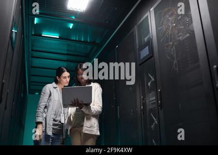 Porträt von zwei weiblichen IT-Technikerinnen, die das Servernetzwerk über einen Laptop einrichten, während sie im Rechenzentrum arbeiten und Platz kopieren Stockfoto