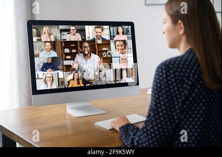 Virtuelle Konferenz, Online-Meeting. Geschäftsfrau, die eine Computer-App nutzt, um mit vielen Menschen gleichzeitig zu kommunizieren. Rückansicht im Büro. Videoanruf mit verschiedenen Mitarbeitern Stockfoto