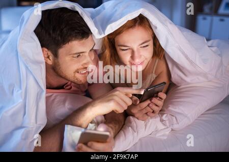 Glückliches Paar mit Smartphones nachts im Bett Stockfoto