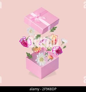 Luxuriöse Geschenkbox mit fliegenden Blüten und Blättern auf hellrosa Hintergrund. Minimales Frühlings- oder Sommerkonzept. Ein modernes lustiges Konzept von Geschenken, Stockfoto