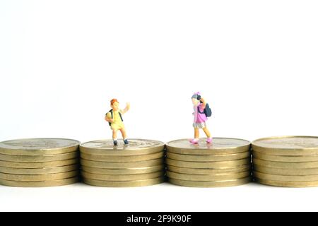 Budget für den Eintritt in die Schule. Kinder oder Kinder, die über den Goldmünzstapel gehen. Miniatur winzigen Menschen Spielzeug Fotografie. Isoliert auf weißem Hintergrund Stockfoto