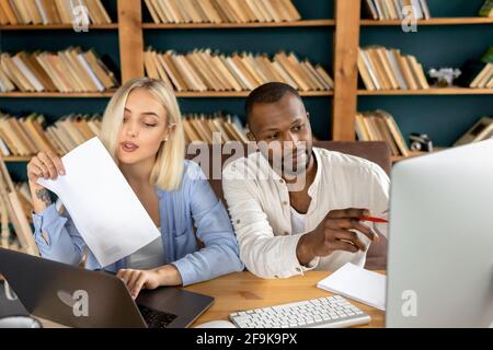 Mixed-Race-Kollegen mit Laptop und Computer, machen einige Papiere, lernen Finanzdiagramme. Stilvolle junge Kollegen diskutieren neue Ideen für Stockfoto