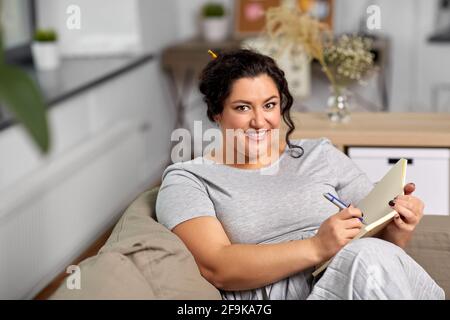 Glückliche junge Frau mit Tagebuch auf dem Sofa zu Hause Stockfoto