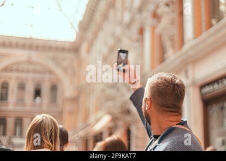 Die Rückansicht eines jungen Mannes aus nächster Nähe fotografiert die Architektur eines Gebäudes oder Wahrzeichen auf seinem Telefon. Stockfoto