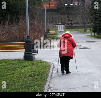 Dnepropetrovsk, Ukraine - 04.08.2021: Müde Frau im reifen Alter geht durch die Stadt. Eine Frau hält Nordic-Walking-Stöcke in den Händen. Stockfoto