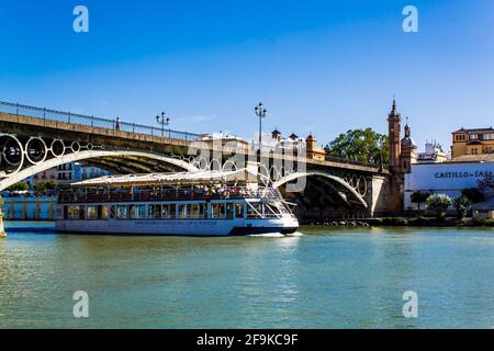 Sevilla, Andalusien, Spanien - 12. Mai 2013: Touristenschiff fährt unter der Brücke von Isabel II (Puente de Isabel II (Puente de Triana)). Stockfoto