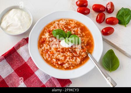 Tomatensuppe mit Reis, verziert mit Rahm und Basilikumblättern. Stockfoto