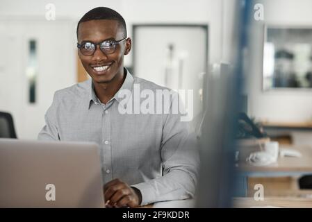 Afrikanischer Geschäftsmann lächelt, während er einen Laptop im Büro benutzt Stockfoto