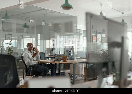 Lächelnder afrikanischer Geschäftsmann, der in einem Büro telefoniert Stockfoto