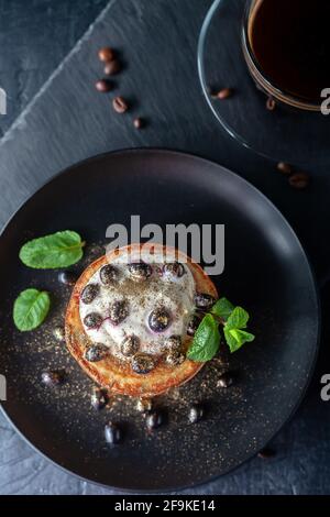 Frisch zubereitete hausgemachte Pfannkuchen mit saurer Creme und frischen Beeren, dekoriert mit Food Gold mit einer Tasse duftenden Kaffee Stockfoto