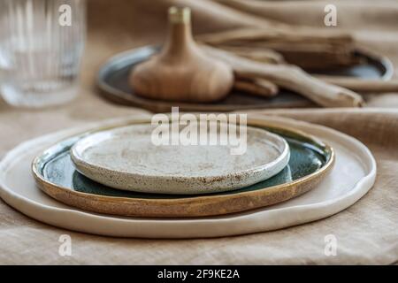 Tischeinstellung mit handgefertigten handwerklichen Tellern auf Leinentischdecke und Holzaccessoires in Erdtönen Stockfoto