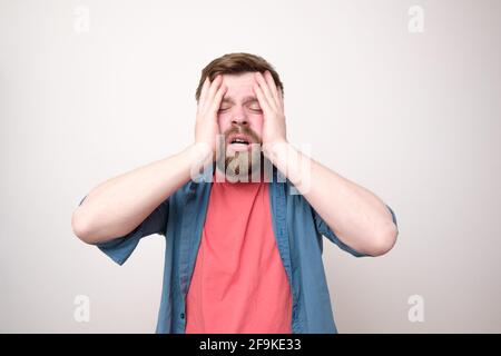Erschöpfter bärtiger Mann müde oder gestresst, hält die Hände auf dem Kopf und die Augen geschlossen. Depression. Kopfschmerzen. Weißer Hintergrund. Stockfoto