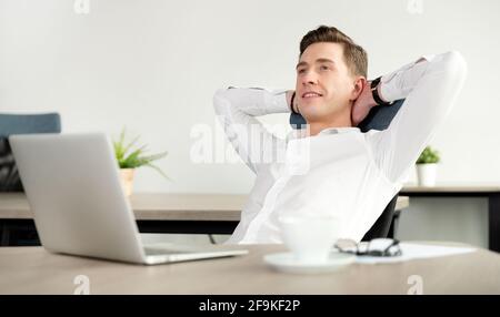 Geschäftsmann, der sich nach einem anstrengenden Arbeitstag im Büro entspannen kann. Fröhlicher Mitarbeiter, der auf einem Stuhl im Büro sitzt Stockfoto