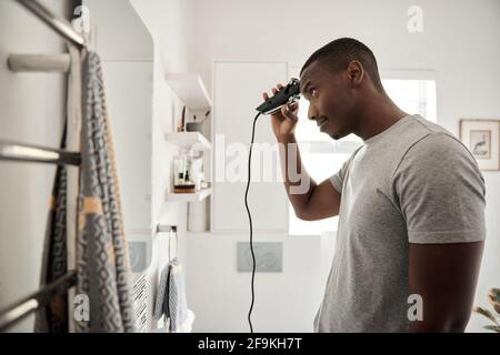 Junger afrikanischer Mann, der sich in seinem Badezimmer die Haare schneidet Stockfoto