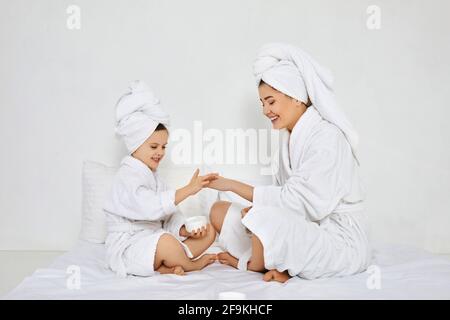 Mutter und Tochter tragen in weißen Bademänteln Creme auf Stockfoto