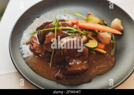 Rindfleisch Bourguignon mit Gemüse auf einem schwarzen Teller Stockfoto