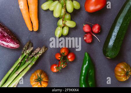 Sortiment von Frühlingsgemüse wie Zucchini und Tomaten auf dunklem Schwarzen Brett. Konzept von Frühlingsessen und Bio-veganer Ernährung Stockfoto