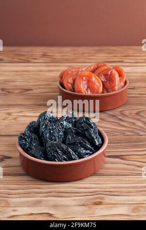 Getrocknete Pflaumen und getrocknete Aprikosen liegen in Keramikschalen auf einem Holztisch. Nahaufnahme. Makro Stockfoto