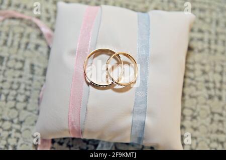 Gold- und Silberring mit Relief auf einem weiteren größeren Ring, die beiden Ringe auf einem schönen weißen Kissen mit blauen und rosa Details. Stockfoto