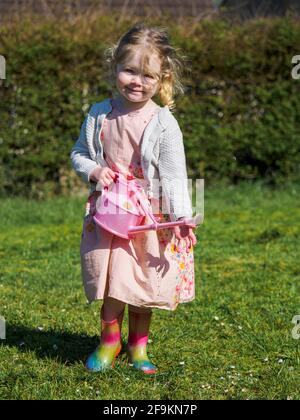 Kleinkind in einem Kleid mit gummistiefeln, Watering Daisies, Großbritannien Stockfoto