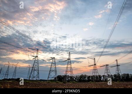 Elektrische Masten und Hochspannungsleitungen im Hintergrund bei Sonnenuntergang. Gruppieren Sie die Silhouette der Sendetürme. Stockfoto