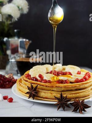 Honig gießt über den Stapel Pfannkuchen mit Banane und Granatapfel Stockfoto