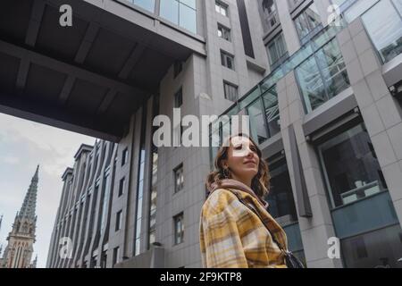 Glückliche Geschäftsfrau in gelbem Mantel geht in ein Business Center in einer Großstadt. Stockfoto