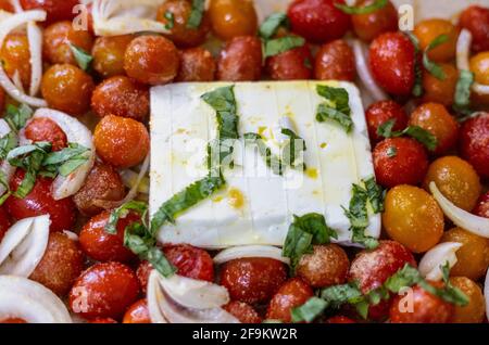 Block von Feta in einem Bett von Kirschtomaten mit Zwiebel, Salz, Olivenöl, Stockfoto