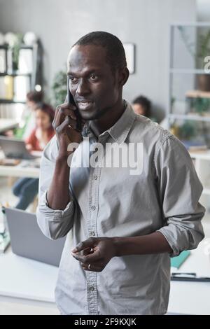 Afrikanischer junger Geschäftsmann diskutiert mit seinem Partner über die Arbeit mit dem Handy Telefonieren, während Sie im Büro stehen Stockfoto