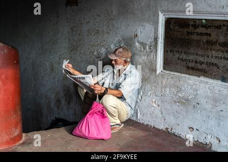 Mysuru, Karnataka, Indien - 2019. Januar: Ein älterer Inder, der allein sitzt und in einem schmuddeligen Korridor eine Zeitung liest. Stockfoto