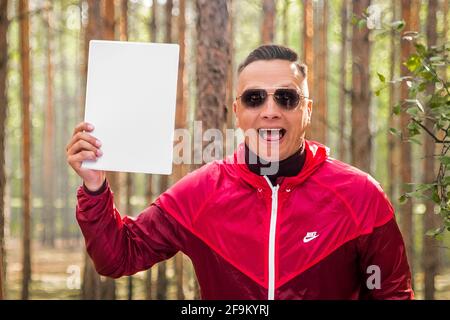 Weißrussland, Region Minsk - 29. Juni 2019: Porträt eines glücklichen lächelnden Mannes mit offenem Mund in Sonnenbrille und roter Jacke, Nachbau. Stockfoto