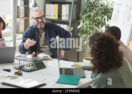 Reifer Geschäftsmann sitzt am Tisch und spricht mit Kollegen Bei Geschäftstreffen im Büro Stockfoto