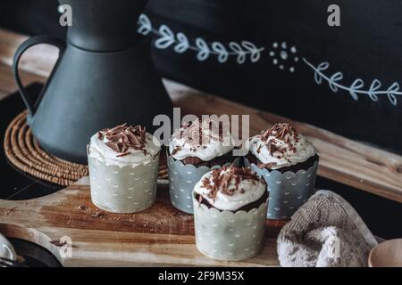 Nahaufnahme von Schokoladen-Muffins mit cremiger Quark-Creme und Schokolade Chips auf schwarzem Hintergrund gestreut Stockfoto