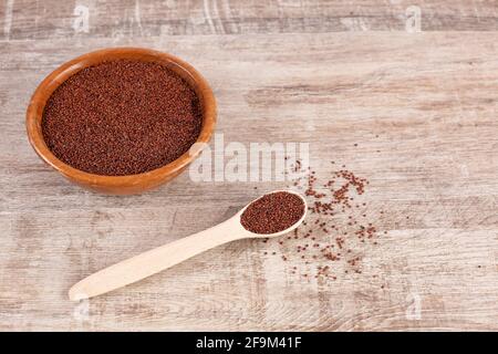 Rote Quinoa-Samen in Holzschüssel und Löffel auf Holzboden. Glutenfreies altes Getreide. Gesunde Ernährung. Stockfoto