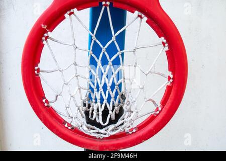 Ein dicker roter Kunststoffring mit weißem Netz, der an einem schwarzen Backboard auf einem Basketballplatz für Kinder befestigt ist. Gedreht in Barbados, Karibik. Heruntergeklappt. Stockfoto