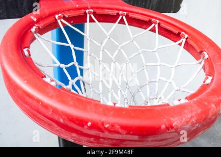 Ein dicker roter Kunststoffring mit weißem Netz, der an einem schwarzen Backboard auf einem Basketballplatz für Kinder befestigt ist. Gedreht in Barbados, Karibik. Stockfoto