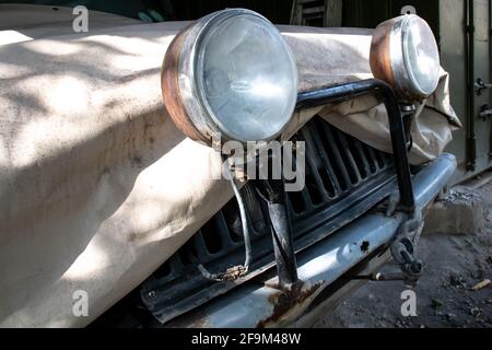 Ein altmodisches Geländefahrzeug, das mit einer beigefarbenen Planenabdeckung aus Segeltuch und externen Halogenkopflampen auf einem Lichtstab-Stoßfänger überzogen ist. Stockfoto