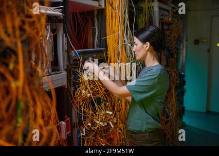 Seitenansicht Porträt einer jungen Frau in Militäruniform Inspektion Server während der Arbeit im Serverraum Stockfoto